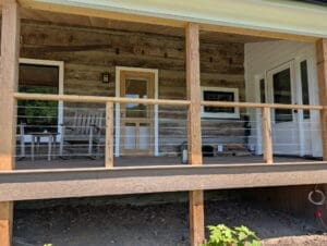 Finished rustic log home porch featuring cable railings and custom columns by an outdoor living contractor in Middle Tennessee.